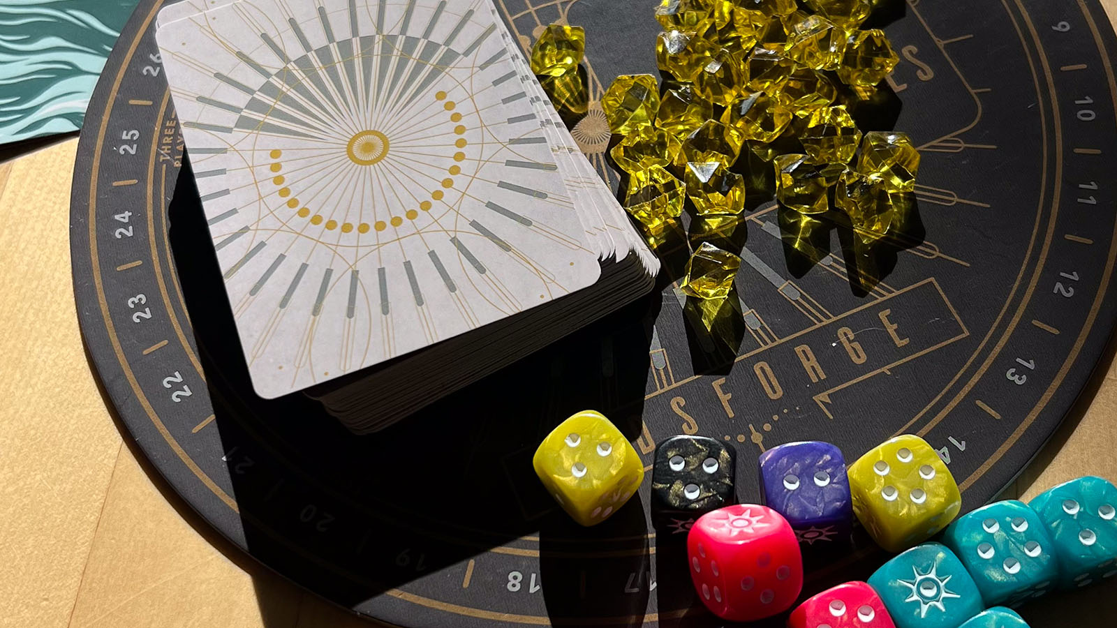 A photo showing the materials that come in the Godsforge game, including a board, dice, and gems.