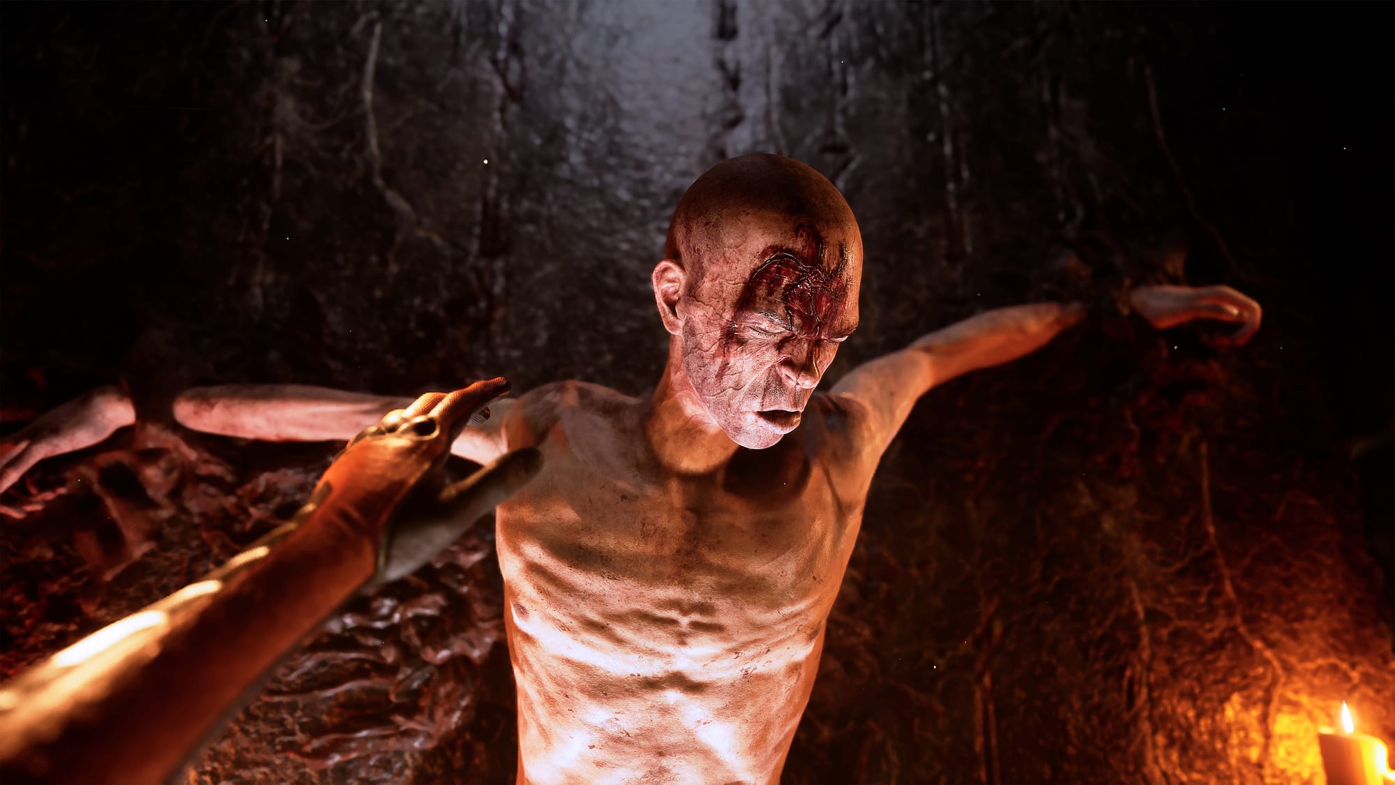 A man tied to a wall. He has a large cut on his forhead that is bleeding heavily. He is shirtless.
