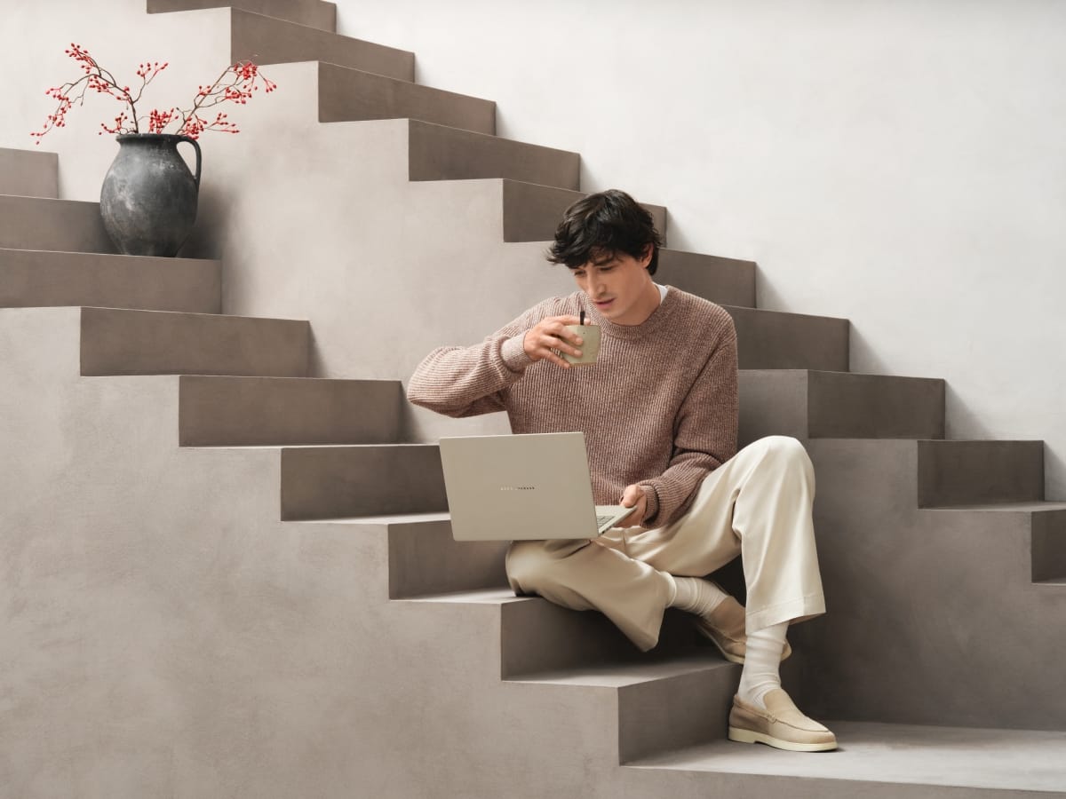 The Zenbook A14 being used by a guy drinking coffee on two sets of stairs.